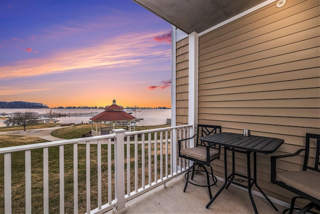balcony at dusk featuring a water view