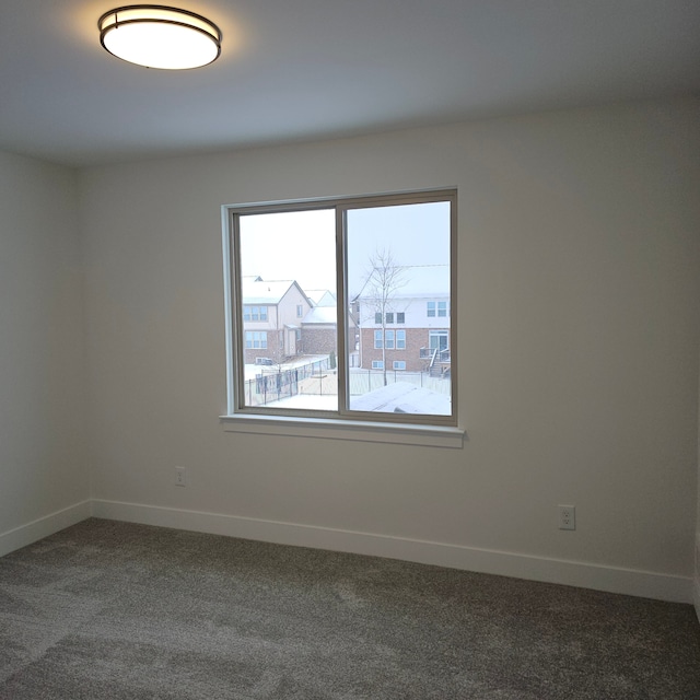 unfurnished room featuring baseboards and dark carpet