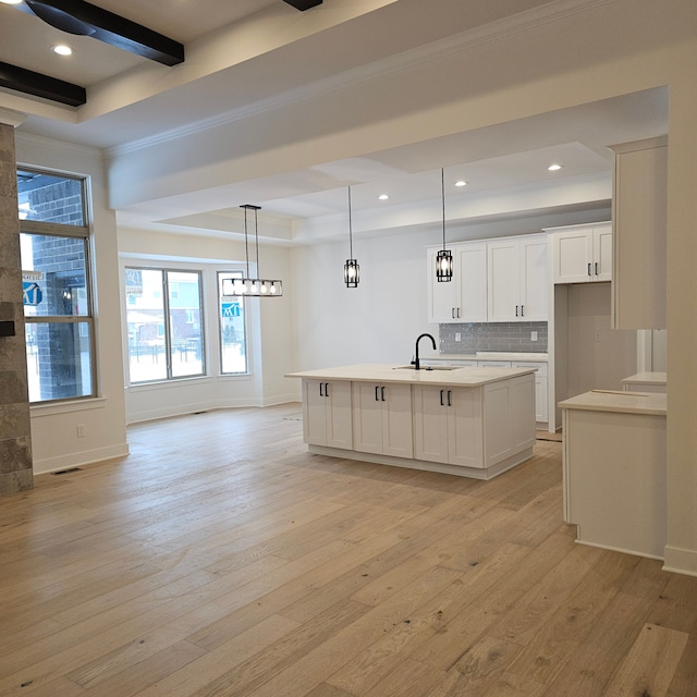 kitchen featuring white cabinets, a sink, light countertops, an island with sink, and backsplash