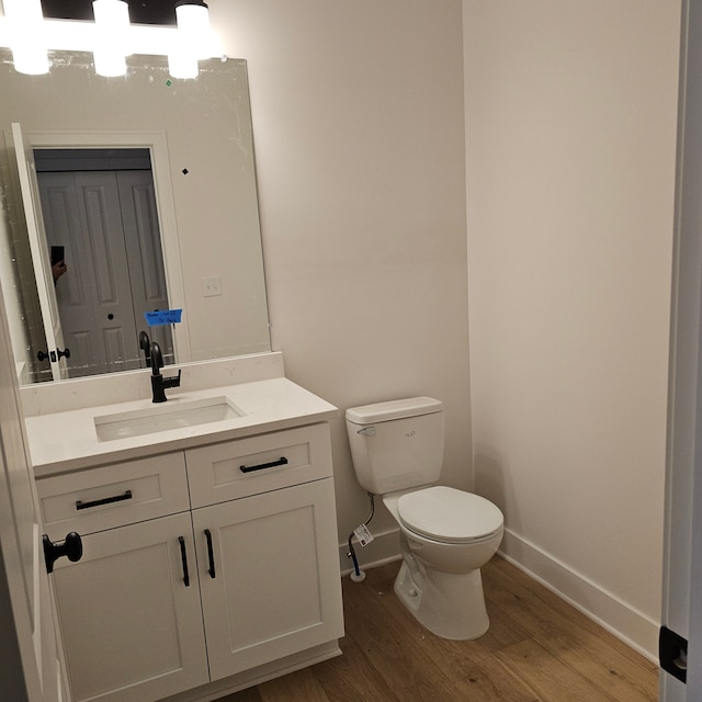 bathroom featuring toilet, baseboards, wood finished floors, and vanity