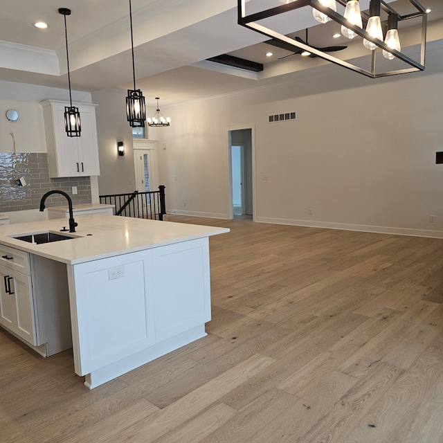 kitchen featuring light wood-type flooring, a sink, light countertops, a chandelier, and white cabinetry
