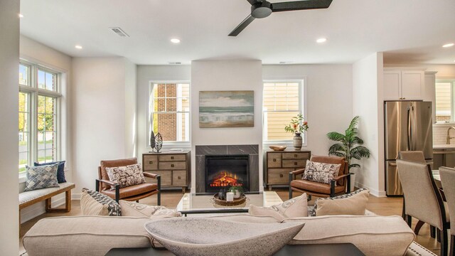 living room featuring recessed lighting, light wood finished floors, a lit fireplace, and ceiling fan