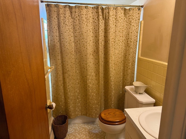 bathroom featuring vanity, tile patterned flooring, toilet, wainscoting, and tile walls