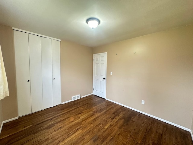 unfurnished bedroom featuring dark wood finished floors, baseboards, and a closet