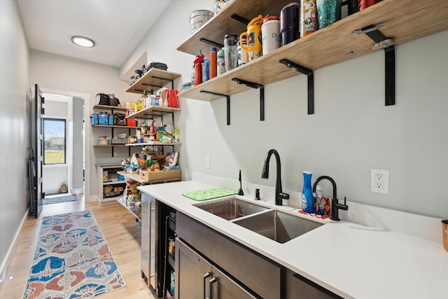 kitchen featuring open shelves, a sink, light wood-style floors, light countertops, and baseboards