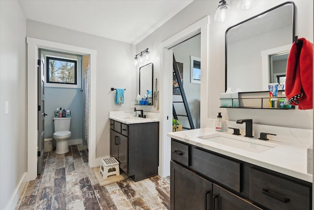 bathroom featuring two vanities, wood finished floors, toilet, and a sink