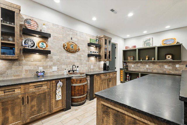 bar featuring visible vents, a sink, light wood finished floors, and decorative backsplash