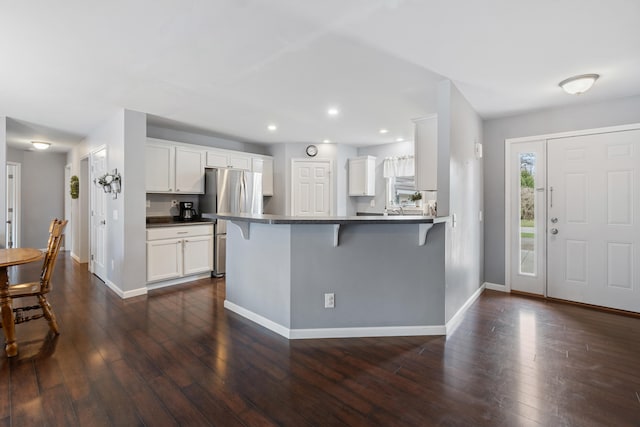 kitchen featuring baseboards, a breakfast bar, freestanding refrigerator, and dark countertops