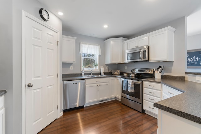 kitchen with appliances with stainless steel finishes, white cabinetry, dark countertops, dark wood finished floors, and a sink