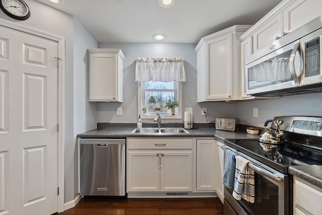 kitchen with a sink, dark countertops, dark wood-style floors, white cabinetry, and stainless steel appliances