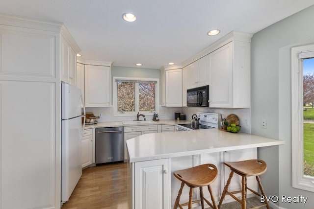 kitchen featuring black microwave, freestanding refrigerator, range with electric stovetop, stainless steel dishwasher, and a sink