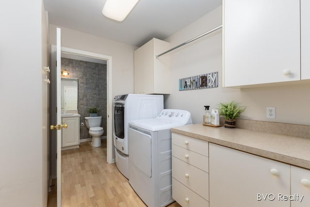 clothes washing area with independent washer and dryer, light wood-style floors, and cabinet space