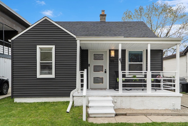 view of front of home featuring roof with shingles, a chimney, and a porch