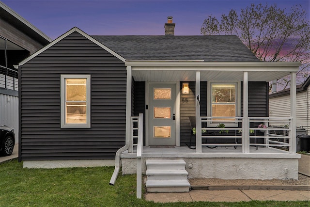 doorway to property with a porch, a chimney, and roof with shingles