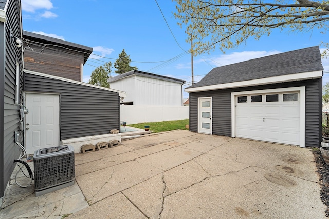detached garage featuring fence, concrete driveway, and central AC