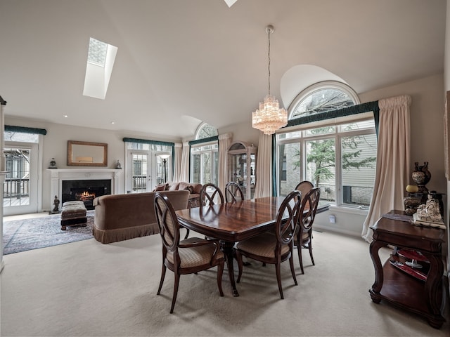 dining space featuring a premium fireplace, light colored carpet, a notable chandelier, and lofted ceiling with skylight