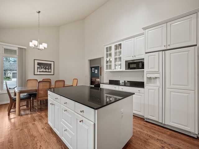 kitchen featuring a notable chandelier, built in appliances, dark countertops, light wood-type flooring, and high vaulted ceiling