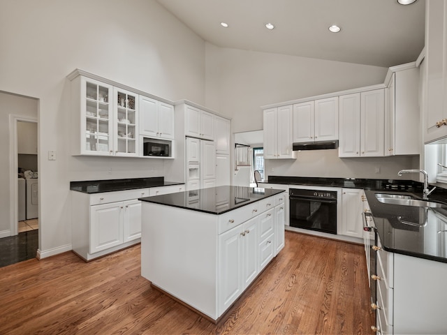 kitchen featuring white cabinets, a sink, under cabinet range hood, black appliances, and washing machine and clothes dryer
