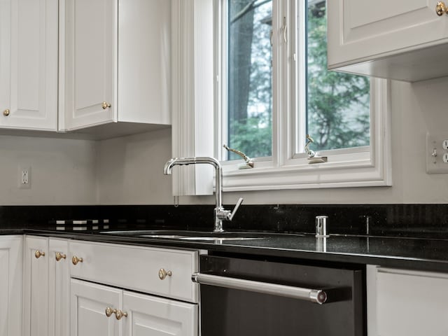 kitchen featuring a sink, dishwasher, dark countertops, and white cabinetry
