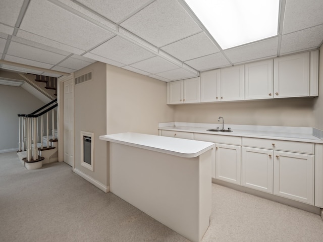 kitchen with visible vents, a sink, light countertops, white cabinetry, and light colored carpet
