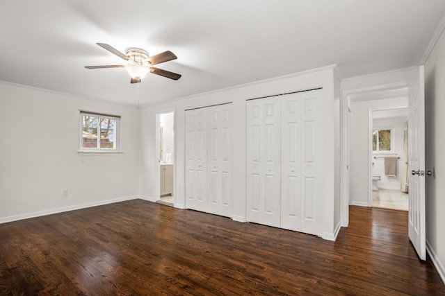 unfurnished bedroom with crown molding, baseboards, dark wood finished floors, and multiple closets