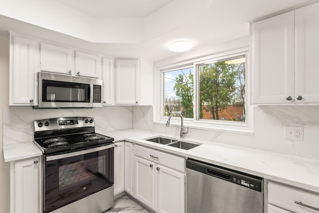 kitchen with white cabinets, light stone countertops, stainless steel appliances, marble finish floor, and a sink