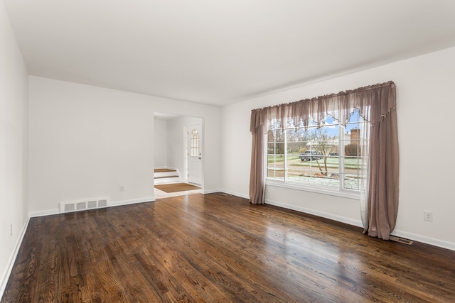 unfurnished room with dark wood-type flooring, visible vents, baseboards, and stairway