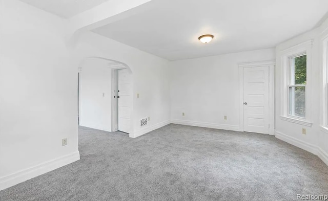 empty room with arched walkways, carpet, and baseboards