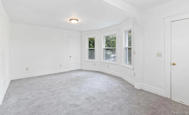 unfurnished room featuring arched walkways, carpet, and baseboards