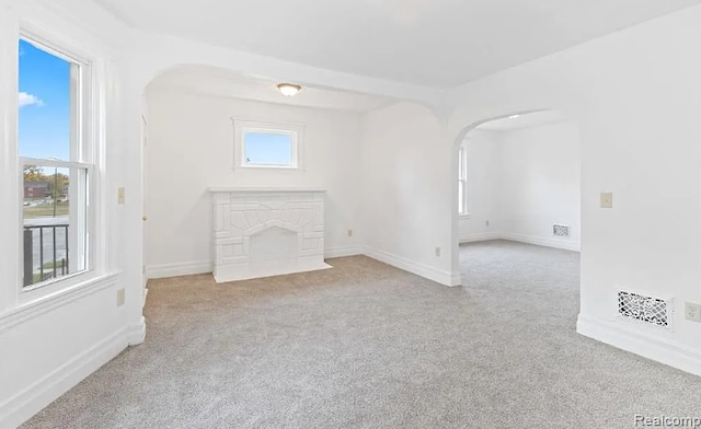 unfurnished living room featuring carpet flooring, baseboards, and arched walkways