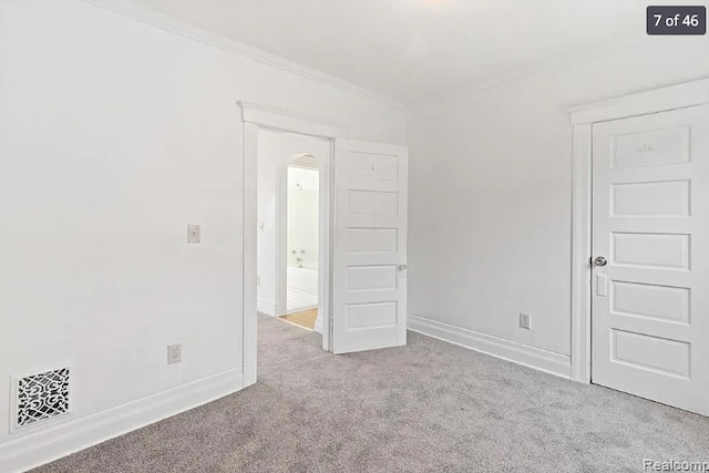 carpeted empty room with arched walkways, baseboards, ornamental molding, and visible vents