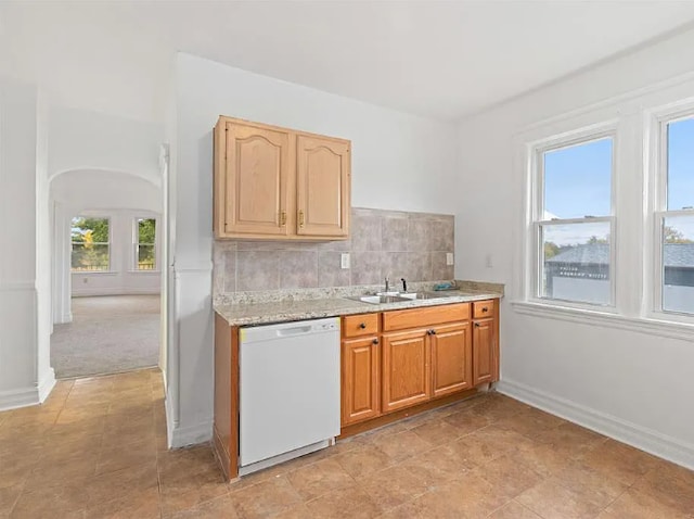 kitchen featuring arched walkways, a sink, white dishwasher, baseboards, and backsplash
