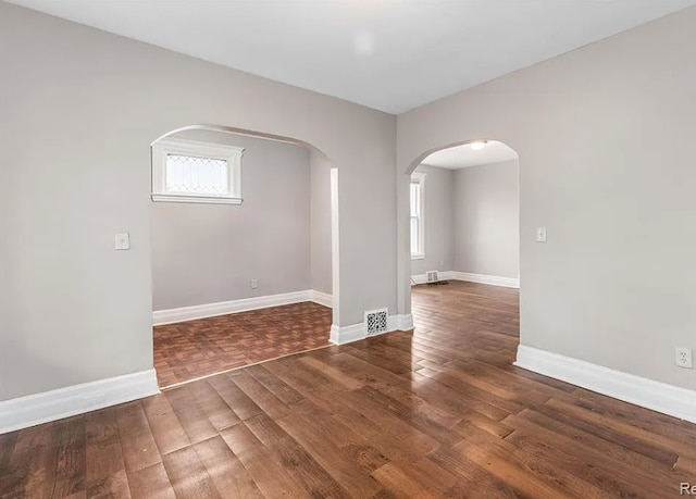 spare room featuring arched walkways, wood finished floors, baseboards, and visible vents