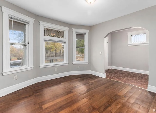 unfurnished room featuring arched walkways, dark wood-type flooring, and baseboards