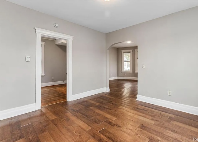 unfurnished room with baseboards, arched walkways, and wood finished floors