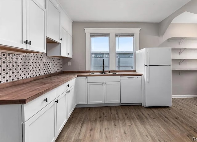 kitchen with white appliances, white cabinetry, decorative backsplash, a sink, and wood finished floors