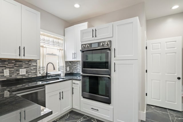 kitchen with recessed lighting, dark stone countertops, marble finish floor, a sink, and stainless steel double oven