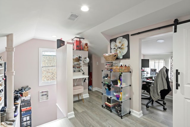 spacious closet with a barn door, visible vents, vaulted ceiling, and wood finished floors