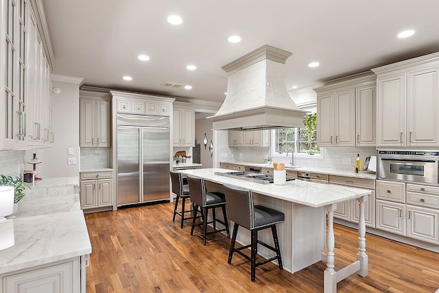 kitchen featuring crown molding, tasteful backsplash, appliances with stainless steel finishes, island range hood, and a breakfast bar area