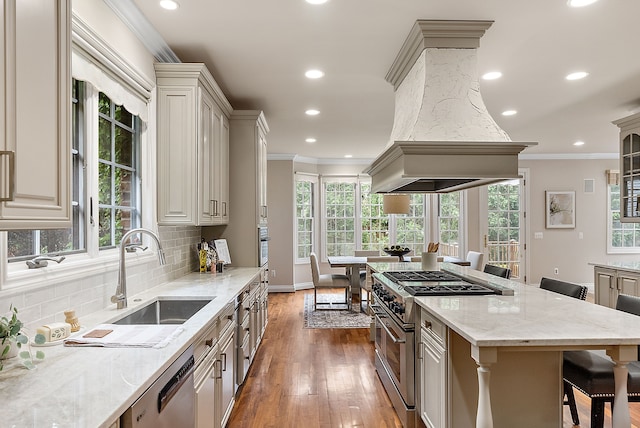 kitchen with island exhaust hood, ornamental molding, a breakfast bar area, appliances with stainless steel finishes, and a sink