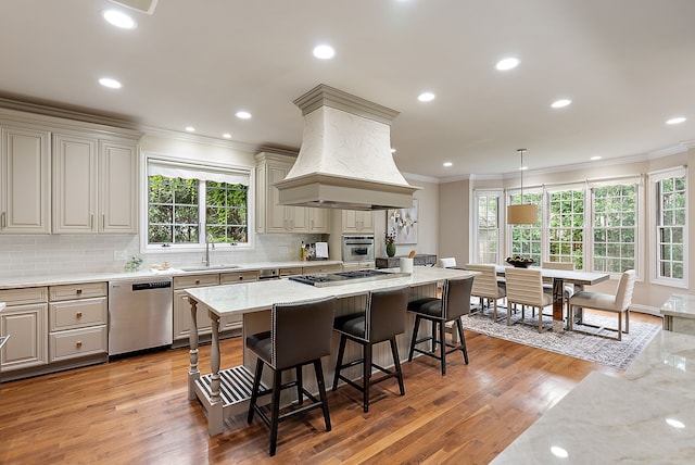 kitchen with a sink, a breakfast bar, crown molding, stainless steel appliances, and custom range hood