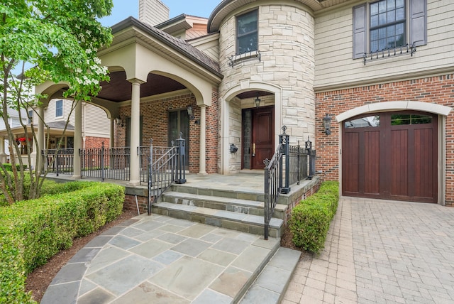 property entrance featuring a garage, brick siding, driveway, and covered porch