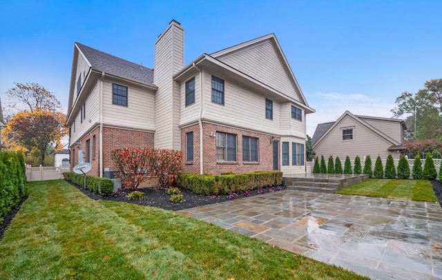 rear view of property featuring brick siding, fence, a yard, and a patio area
