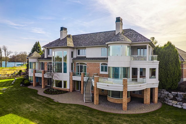 82 Chateaux Du Lac, Fenton, MI 48430 - back of house with brick siding, a chimney, a balcony, a lawn, and a patio
