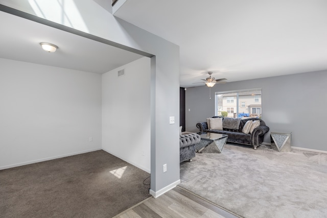 carpeted living room with visible vents, baseboards, a ceiling fan, and wood finished floors