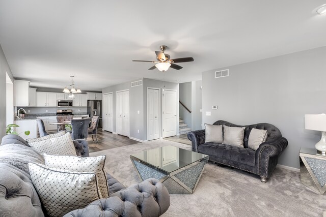 living room featuring visible vents, baseboards, stairway, and ceiling fan with notable chandelier