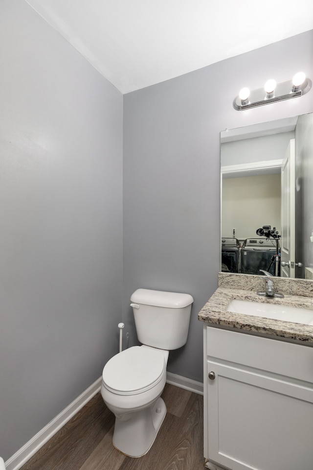 half bath with vanity, toilet, wood finished floors, baseboards, and washer and clothes dryer