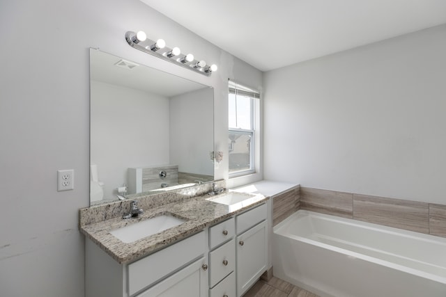 bathroom featuring a bath, double vanity, visible vents, and a sink