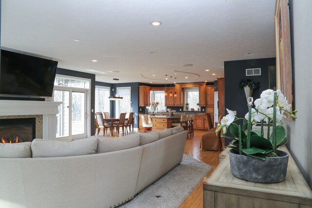 living room with a glass covered fireplace, recessed lighting, light wood-style floors, and visible vents