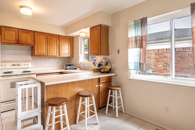 kitchen with white range with electric cooktop, a sink, light countertops, light tile patterned floors, and backsplash